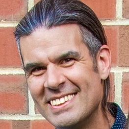 A headshot of a handsome gentleman in fromt of a brick wall.